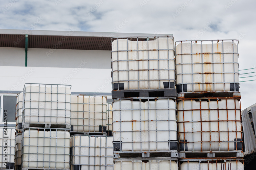 stacked IBC containers with factory background. reuse white plastic chemical tanks in factory
