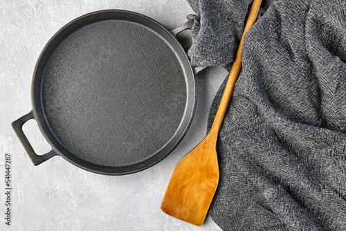 Black cast iron empty frying pan, wooden spatula and gray kitche