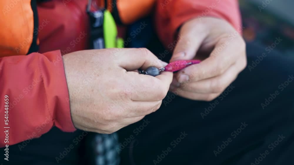 A man puts a vibrotail on a hook, close-up. Preparation of fishing equipment. A man puts a vibrotail on a hook, close-up. Preparation of fishing equipment.