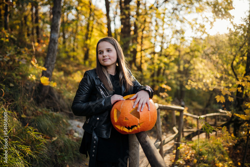 Teenage girl in an autumn park with a pumpkin on Halloween