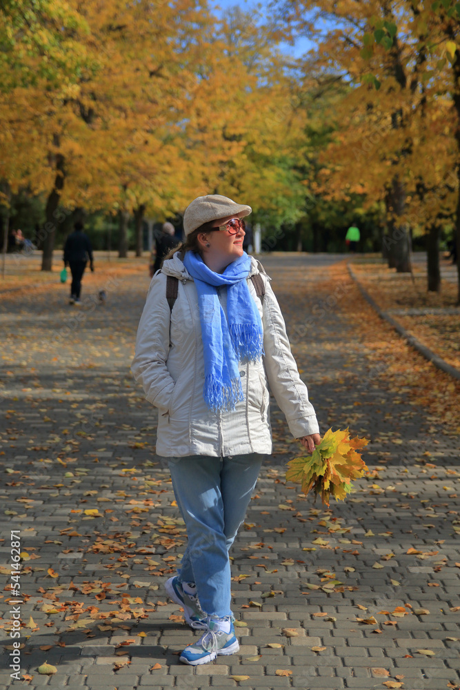 A young woman walks in the autumn park with a bouquet of yellow leaves. A young woman walks in the autumn park with a bouquet of yellow leaves.