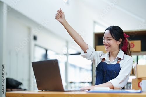 Starting small business entrepreneur of independent Asian woman smiling using computer laptop with cheerful success of online marketing package box items and SME delivery concept