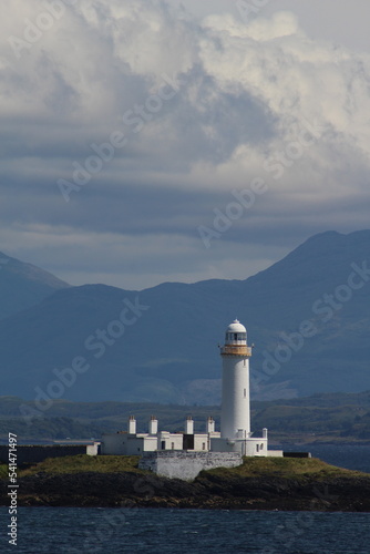 Vertical shot of the lonely lighthouse surrounded by water and mountains