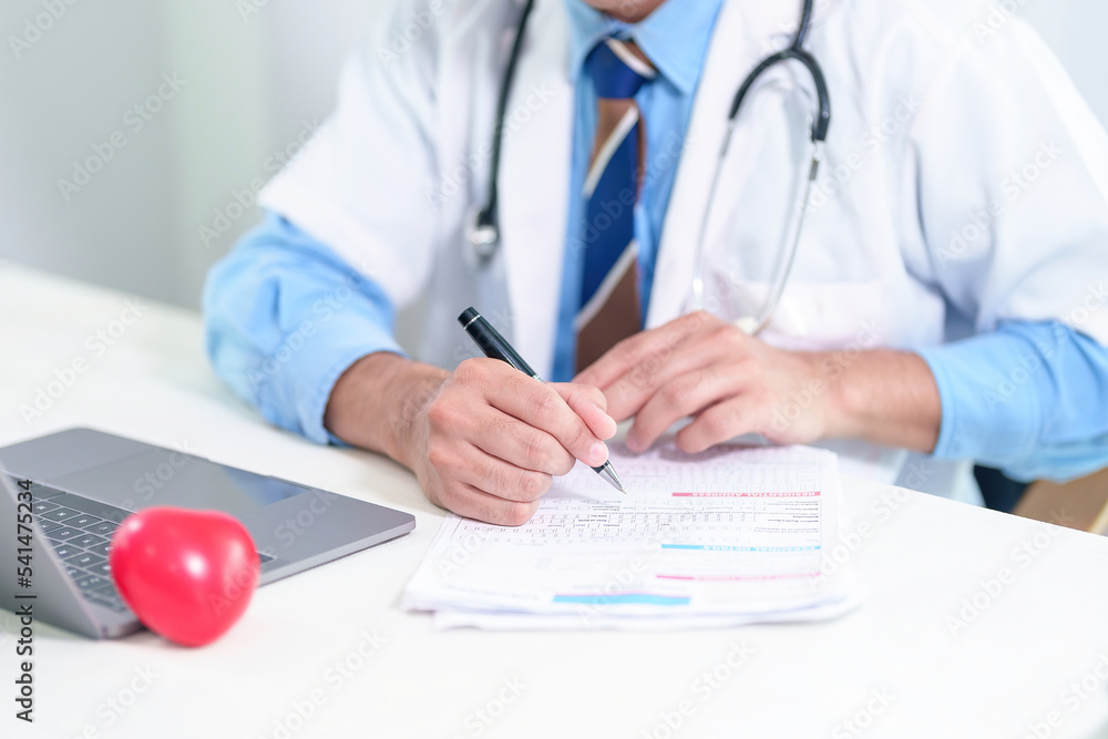 Senior doctor physician using laptop, writing prescription with stethoscope on desk. Old male professional therapist wearing white coat working in hospital. Healthcare, medicine concept. Close up view Senior doctor physician using laptop, writing prescription with stethoscope on desk. Old male professional therapist wearing white coat working in hospital. Healthcare, medicine concept. Close up view