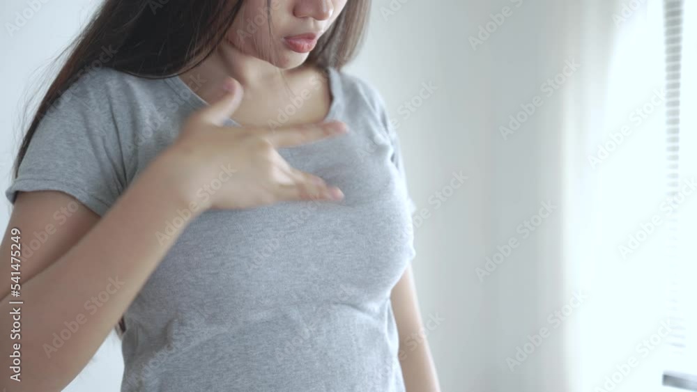 Asian woman wearing a gray T-shirt is self-checking for breast cancer at home. Asian woman wearing a gray T-shirt is self-checking for breast cancer at home.