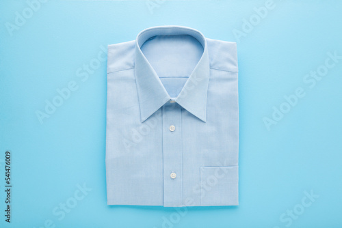 Folded classic shirt on light blue table background. Pastel color. Closeup. Top down view. Male clothes.