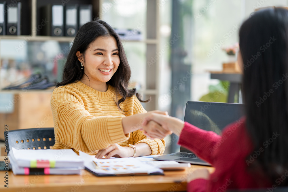 Two young Asian businesswomen shaking hands in a successful business in finance co-investment banking agreement concept. Two young Asian businesswomen shaking hands in a successful business in finance co-investment banking agreement concept.