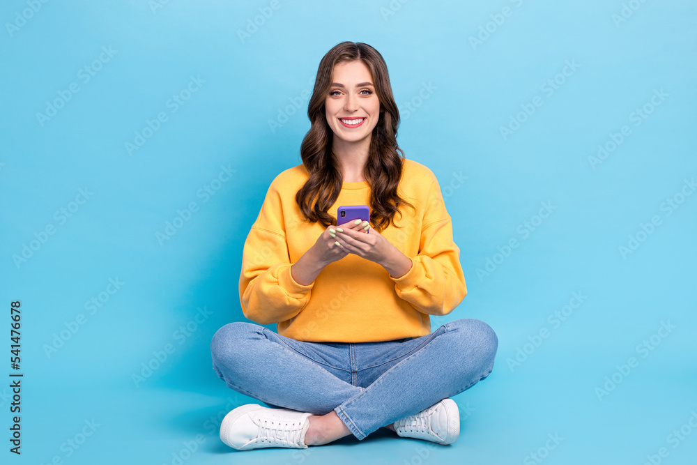 Full length photo of sweet funny lady wear yellow sweater chatting modern device sitting legs crossed isolated blue color background Full length photo of sweet funny lady wear yellow sweater chatting modern device sitting legs crossed isolated blue color background