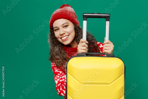 Traveler fun woman wear red cozy knitted sweater hat hold suitcase isolated on plain dark green background studio Tourist travel abroad in free spare time rest getaway Air flight trip journey concept #541477041