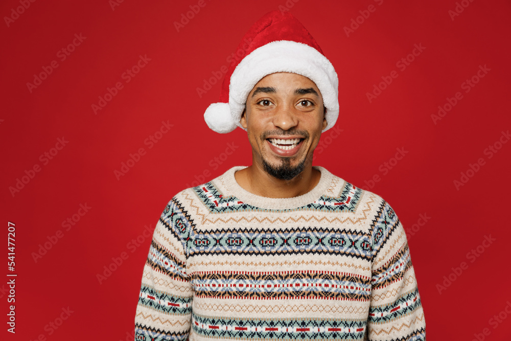 Merry young smiling cool cheerful fun man wear warm cozy Christmas sweater Santa hat posing look camera isolated on plain red color background studio. Happy New Year 2023 celebration holiday concept. Merry young smiling cool cheerful fun man wear warm cozy Christmas sweater Santa hat posing look camera isolated on plain red color background studio. Happy New Year 2023 celebration holiday concept.