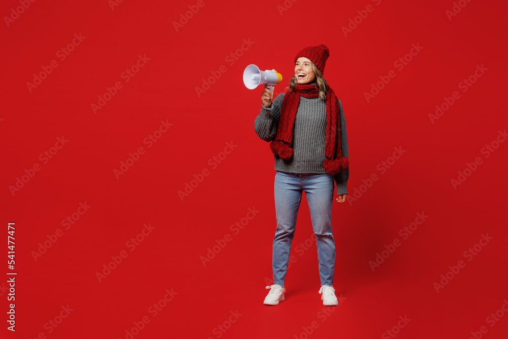 Full body young woman wear grey sweater scarf hat hold scream in megaphone healthcare information isolated on plain red background studio. Healthy lifestyle sick disease treatment cold season concept. Full body young woman wear grey sweater scarf hat hold scream in megaphone healthcare information isolated on plain red background studio. Healthy lifestyle sick disease treatment cold season concept.