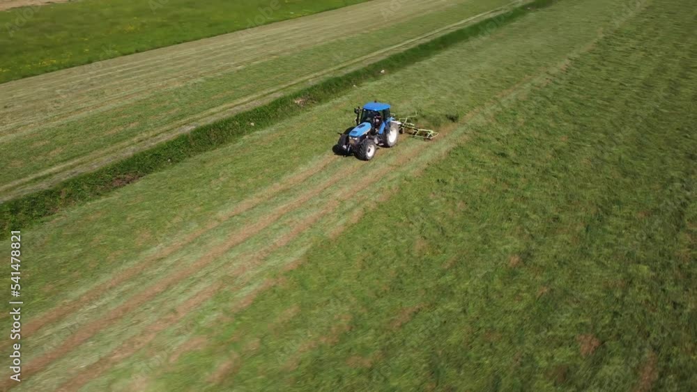 Raking hay with a double wheel rake tractor on a sunny day aerial view Raking hay with a double wheel rake tractor on a sunny day aerial view