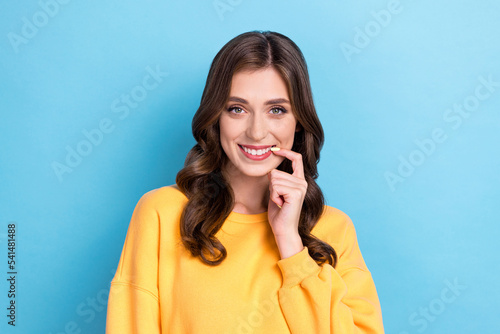 Photo portrait of charming young girl bite nail smiling flirty interested look wear trendy yellow clothes isolated on blue color background