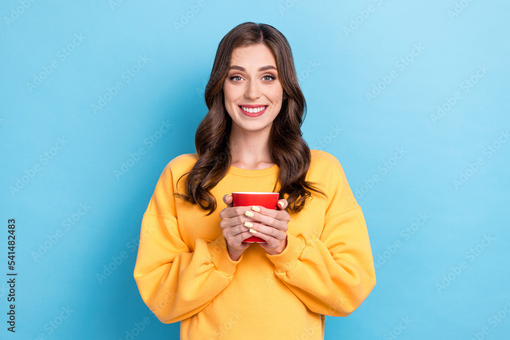 Photo portrait of winsome young woman hold red coffee tea mug cup enjoy cacao wear trendy yellow clothes isolated on blue color background Photo portrait of winsome young woman hold red coffee tea mug cup enjoy cacao wear trendy yellow clothes isolated on blue color background