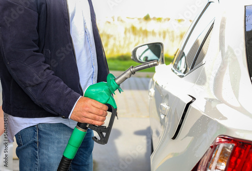 Man holding gasoline fuel nozzle to refuel benzine gas into vehicle petrol station, day light. Transportation and ownership concept. 