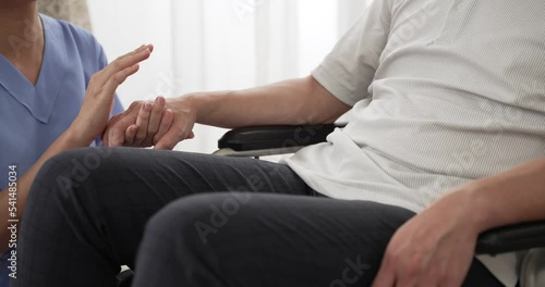 closeup with selective focus of hands of nursing aide holding and patting winkled hand of a patient on wheelchair. Domiciliary care for sick elderly people concept