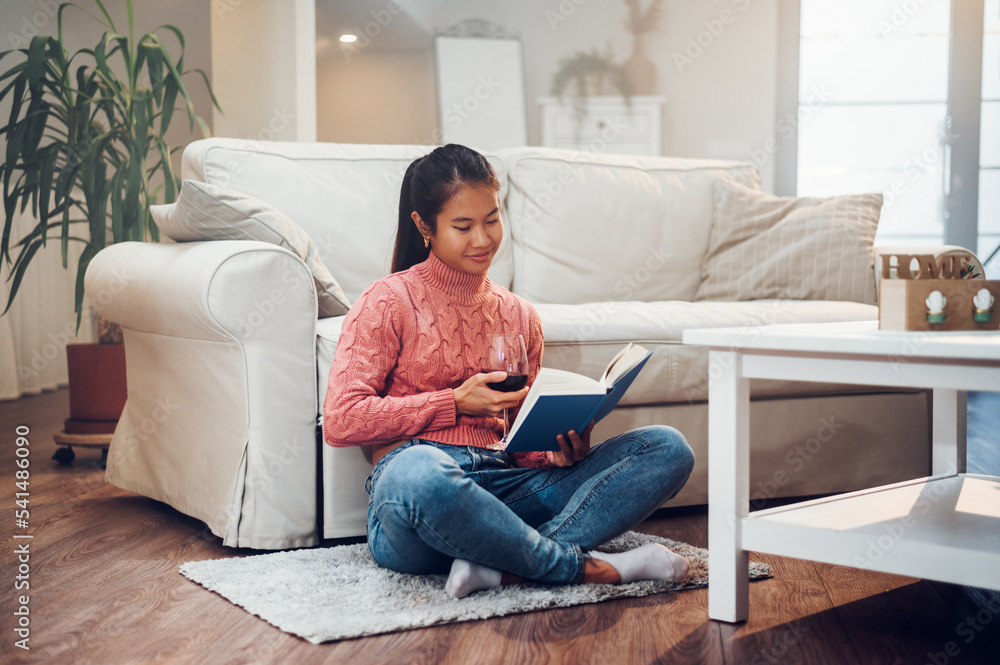 Asian woman sitting on the floor while reading a book and drinking wine Asian woman sitting on the floor while reading a book and drinking wine