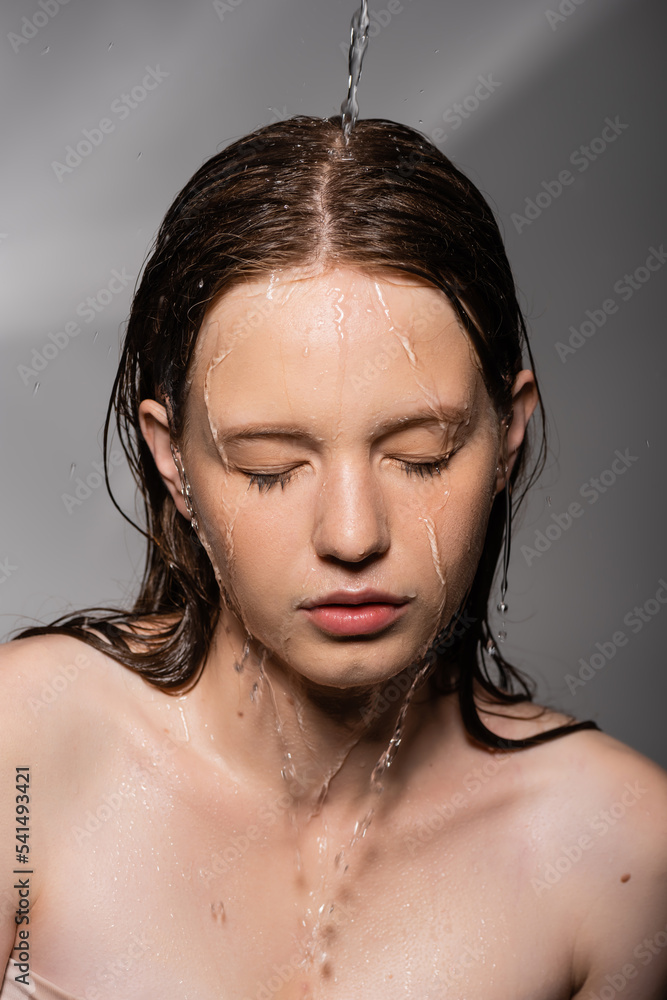Water pouring on hair and face of young model on grey background Stock