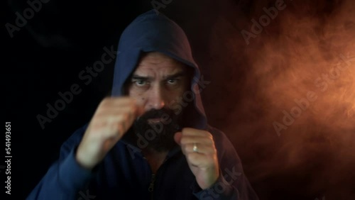 Boxer training wearing hoodie in low light gym in slow motion in the smoke. Fighter punching without gloves. photo