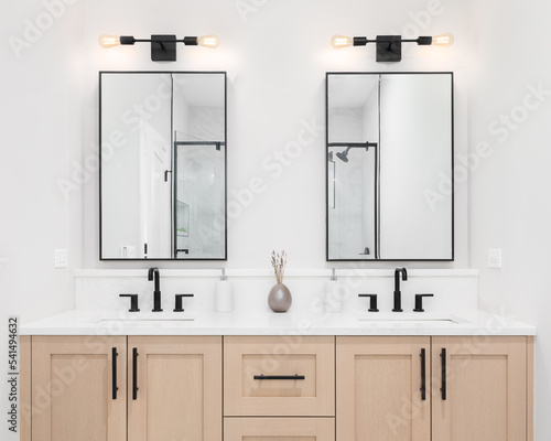 Fotografie A modern bathroom with a wooden vanity cabinet, black faucets, white marble countertop, and black rimmed square mirrors