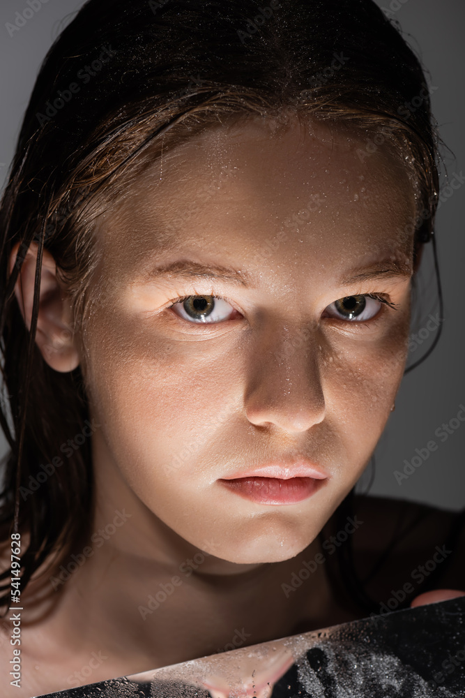 Portrait of woman with wet skin looking at camera near mirror with light isolated on grey