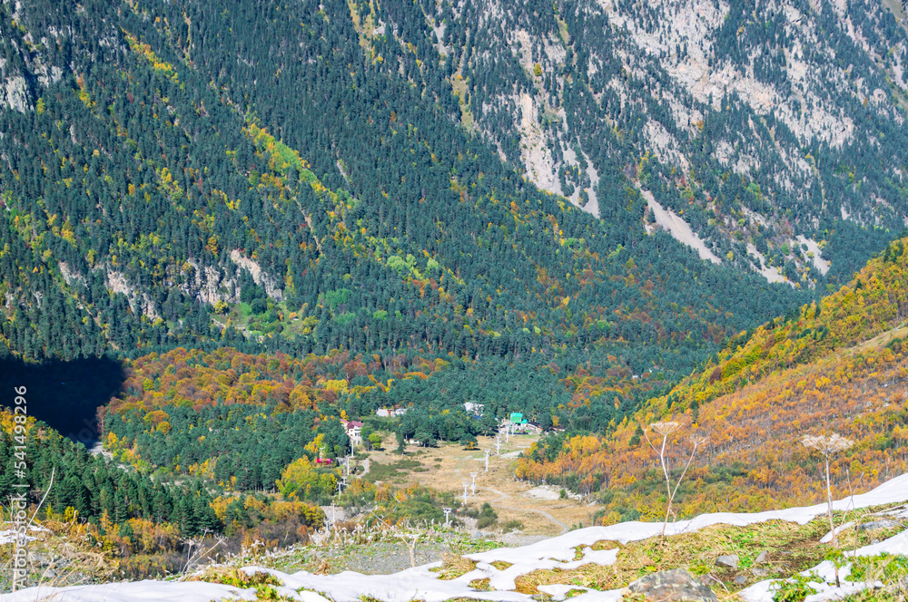 Panorama with mountain view. View of the mountain peaks. Snow in the mountains. Nature in the mountains. Snow-capped mountain peaks. The multi colored color of trees in autumn in a mountainous area.