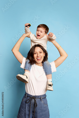 Little boy act up and cry. Young mother with little kid isolated on blue background. Concept of emotions, Mother's Day, love, family and parenthood