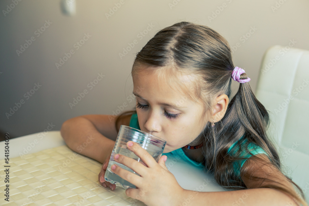 Beautiful little girl drinks clean water from a transparent glass. Beautiful little girl drinks clean water from a transparent glass.