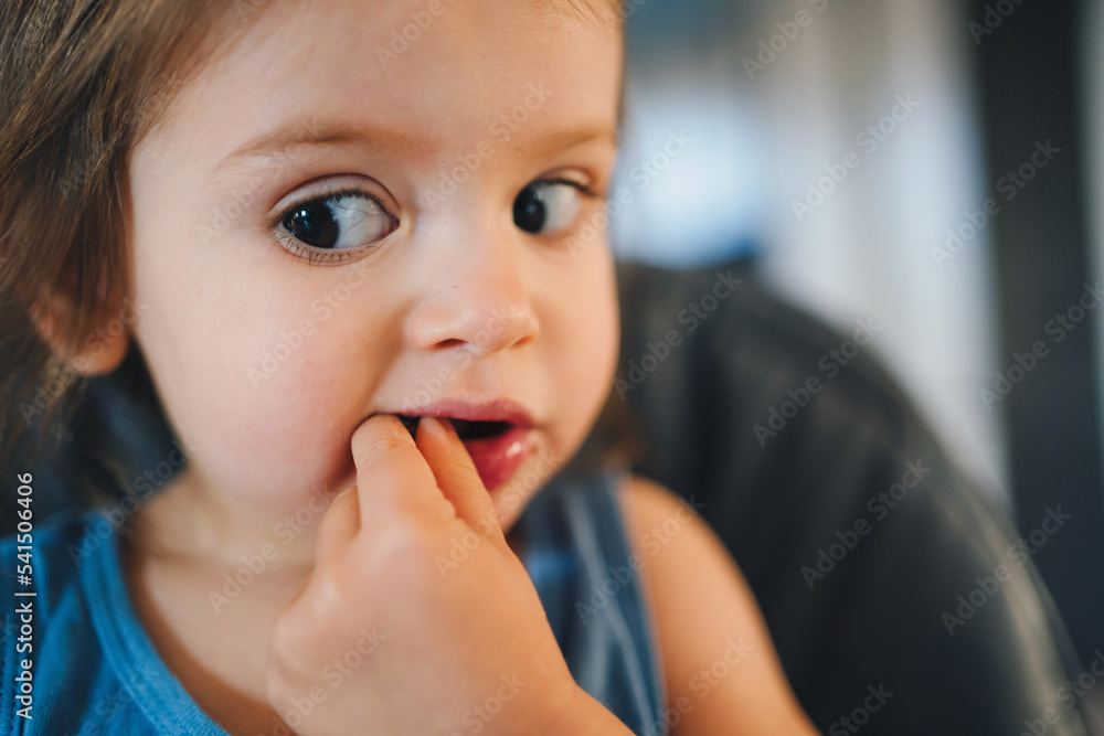 Baby girl sitting on high-chair eating while looking with big brown eyes in the side. Healthy eating. Child health care. Sweet food. Baby girl sitting on high-chair eating while looking with big brown eyes in the side. Healthy eating. Child health care. Sweet food.