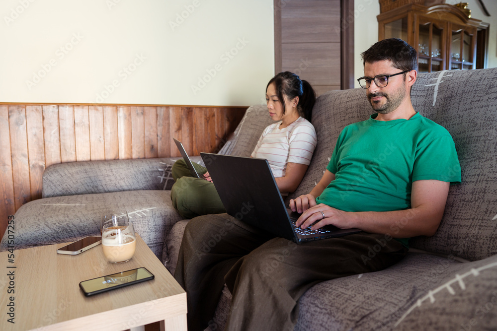 Serious couple sitting with laptops on sofa in living room Serious couple sitting with laptops on sofa in living room