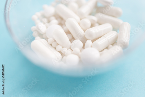 Different white pills and a plastic container on a blue background. Medical theme. 