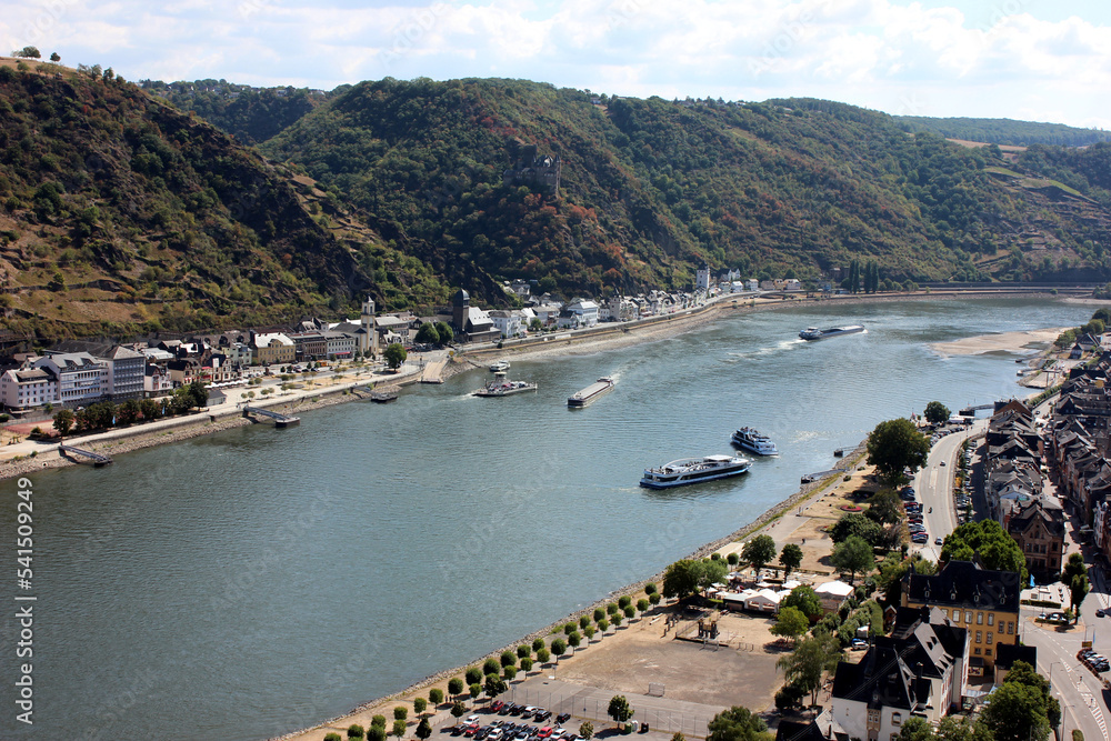 Barge with a covered deck sailing on the river Rhine in western Germany, visible buildings on the river bank, aerial view.