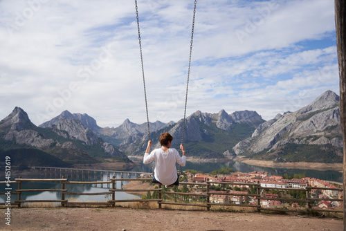 Blonde woman swinging on a giant wooden swing, in front of the amazing mountainous landscape of the Riaño damming in León, Spain.