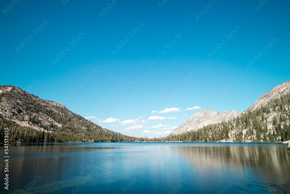 Toxaway Lake, located in Idaho’s Sawtooth Wilderness seen on a summer day, with a blues sky, white clouds and a reflection in the calm waters of the pristine alpine lake.