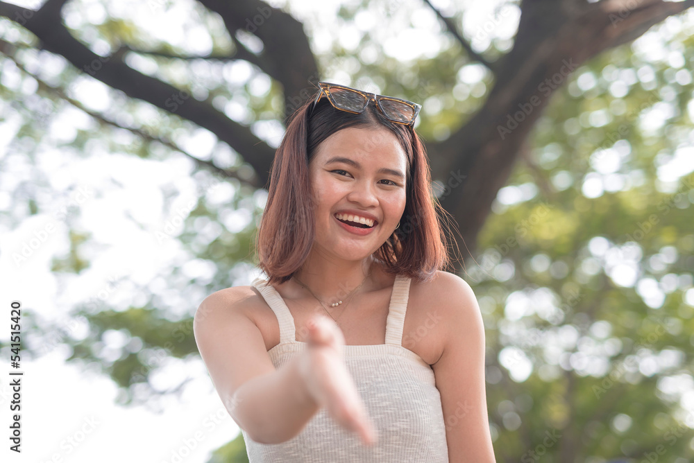 A Southeast Asian lady smiles brightly and extends her arm as she initiates a handshake. A Southeast Asian lady smiles brightly and extends her arm as she initiates a handshake.