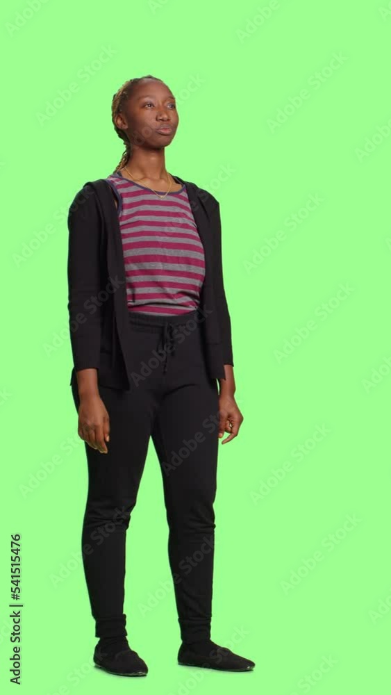 Vertical video: Young adult looking at hologram over green screen backdrop, using holographic image and artificial intelligence. Female model standing on full body isolated greenscreen background. Vertical video: Young adult looking at hologram over green screen backdrop, using holographic image and artificial intelligence. Female model standing on full body isolated greenscreen background.