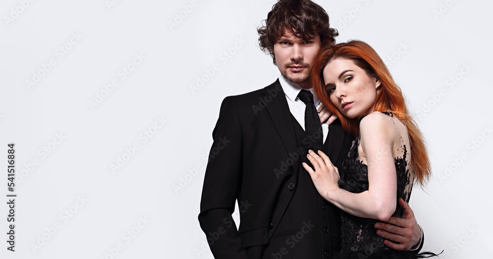 Sexy bright foxy hairstyle female woman in fashion black long skirt wedding dress hugging her handsome man in black luxury suit clothing isolated on white background with empty copy space. Closeup Sexy bright foxy hairstyle female woman in fashion black long skirt wedding dress hugging her handsome man in black luxury suit clothing isolated on white background with empty copy space. Closeup