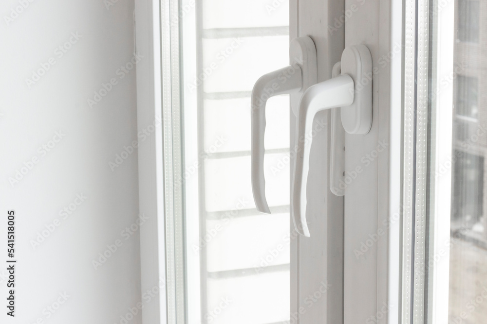 White plastic window handles detail, closeup view, horizontal photo. Closed modern windows in flat, PVC plastic, handles turned down side view, cold weather