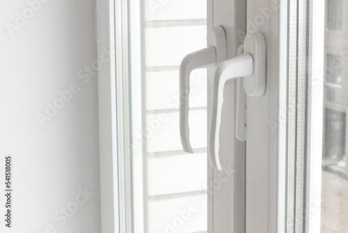 White plastic window handles detail, closeup view, horizontal photo. Closed modern windows in flat, PVC plastic, handles turned down side view, cold weather (ID: 541518005)