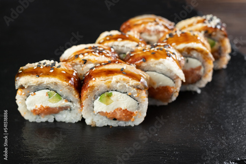 sushi roll with avocado, eel, sesame seeds, sauce and tobiko caviar on black background. Japanese cuisine, restaurant service. Sushi menu