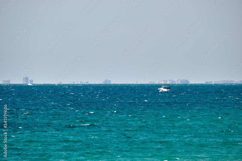 Sea panorama. Small motor boat floats in deap blue bay water under bright blue sky, tall buildings on distant shore