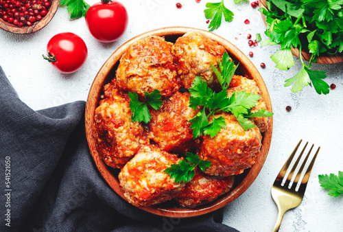Meatballs in tomato sauce in wooden bowl on white kitchen table background, spices and herbs. Delicious home cooking. Top view
