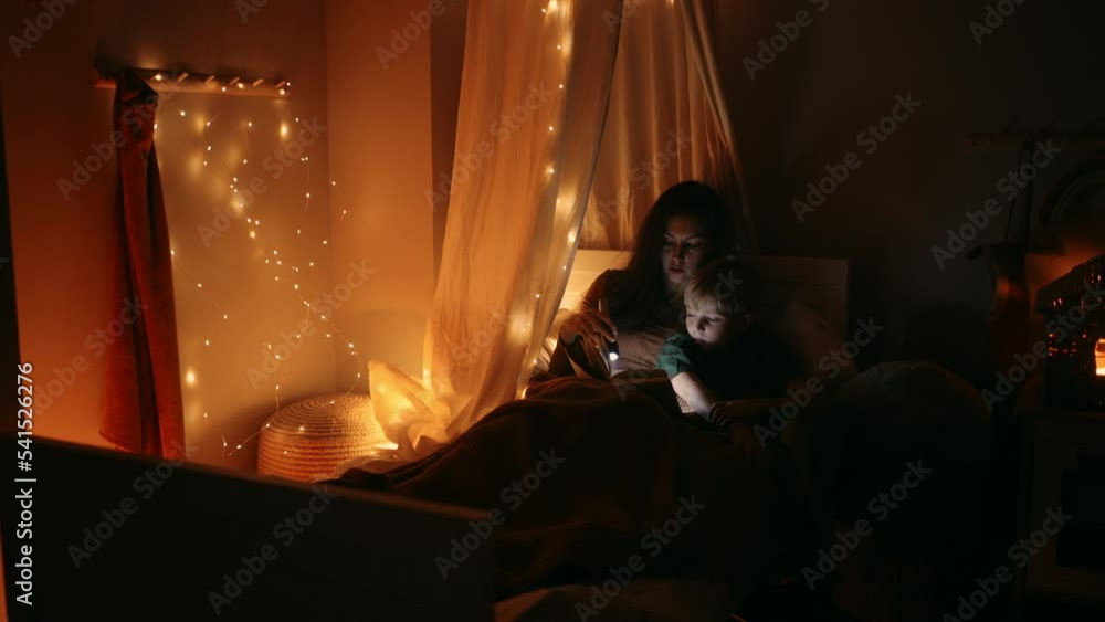 a mother lying in bed with his son reads him a fairy tale before going to bed with a lantern. read a book with my son, a lullaby. Mother and son in bed. Children's room, to fall asleep, to put to bed a mother lying in bed with his son reads him a fairy tale before going to bed with a lantern. read a book with my son, a lullaby. Mother and son in bed. Children's room, to fall asleep, to put to bed