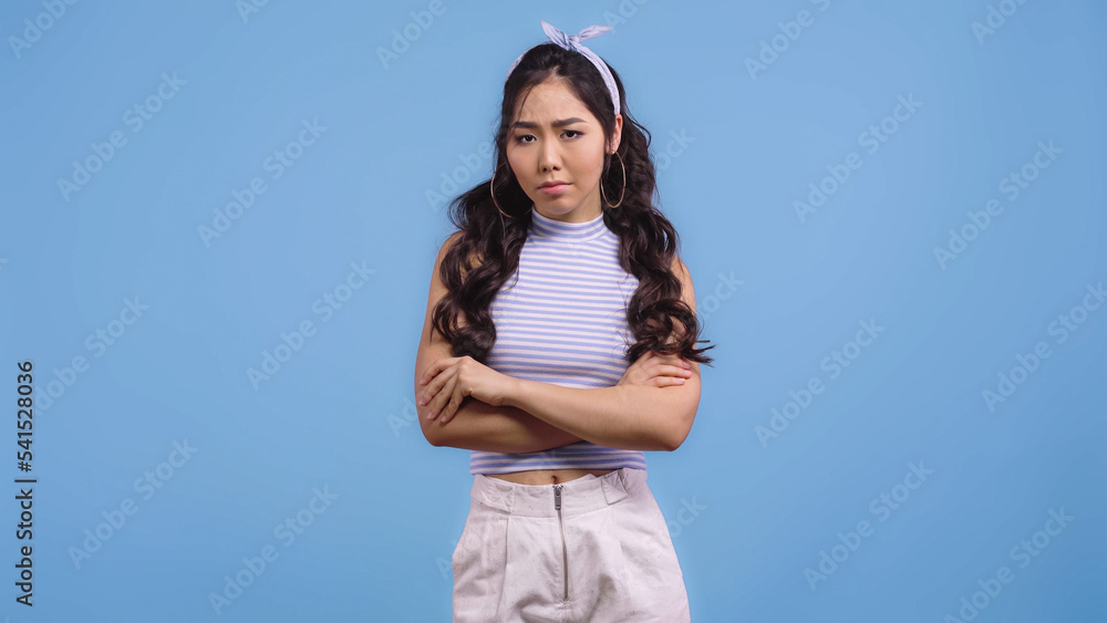 sad asian woman in headband with bow standing with crossed arms isolated on blue sad asian woman in headband with bow standing with crossed arms isolated on blue