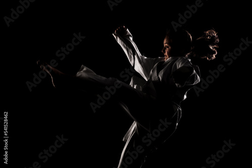 Young girl exercising karate. Child in kimono against black background. © Nikola Spasenoski