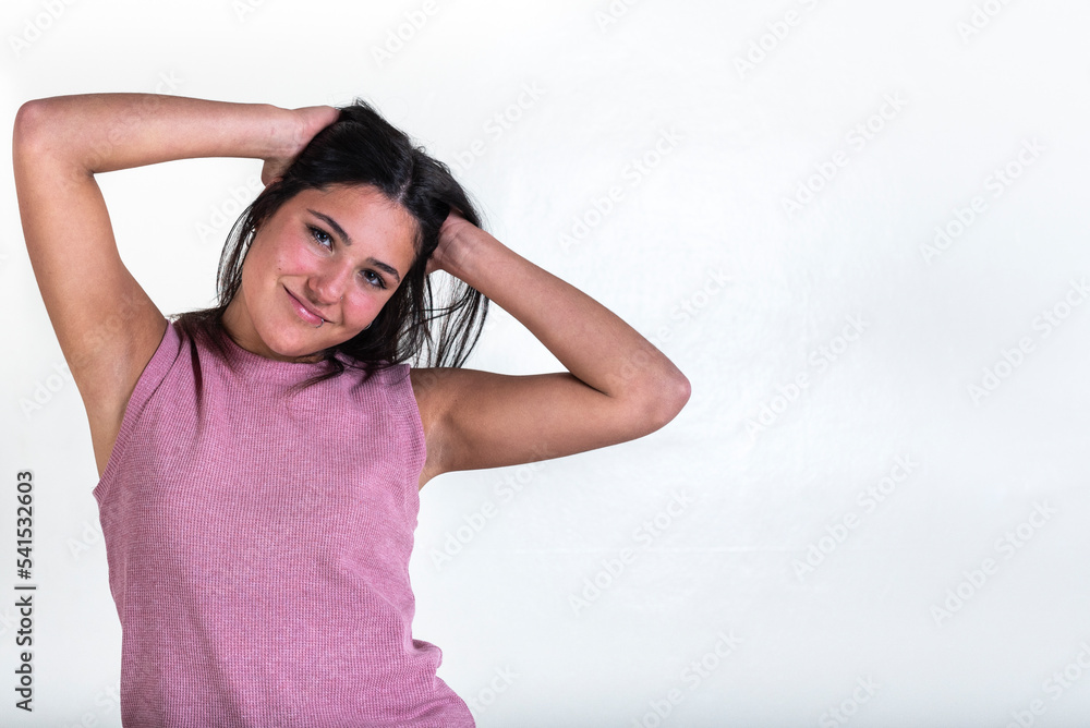 Beautiful young smiling woman wearing a pink t-shirt and with hands on her hair while she is looking at the camera over white background. Copy Space. Beautiful young smiling woman wearing a pink t-shirt and with hands on her hair while she is looking at the camera over white background. Copy Space.