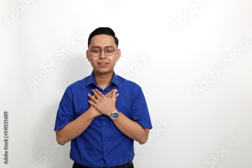 Young asian man standing while touching or holding his chest and close his eyes. He feels relieved and peaceful