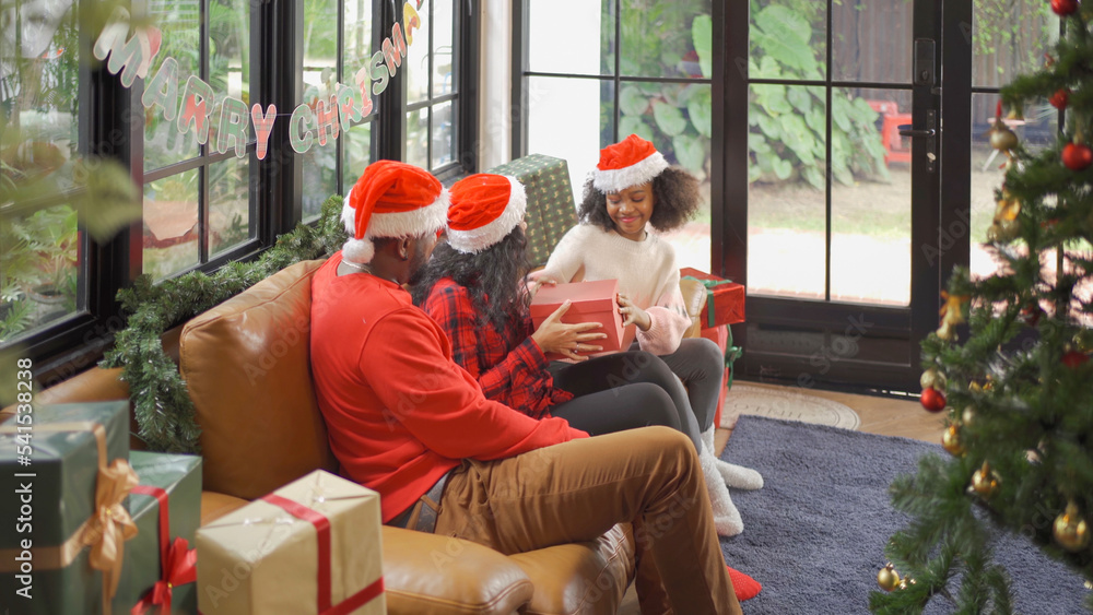 Obraz premium An African American black family, woman, father, mother and kid girl with present gift in party on Merry Christmas Eve Xmas on holiday. Celebration at home. People lifestyle.