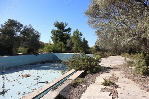 Lost places: views of an empty pool from a not abandoned hotel complex in Izmir, Turkey. The swimming area is left to decay and already overgrown by nature. Forgotten ruins in a vacation paradise. photo