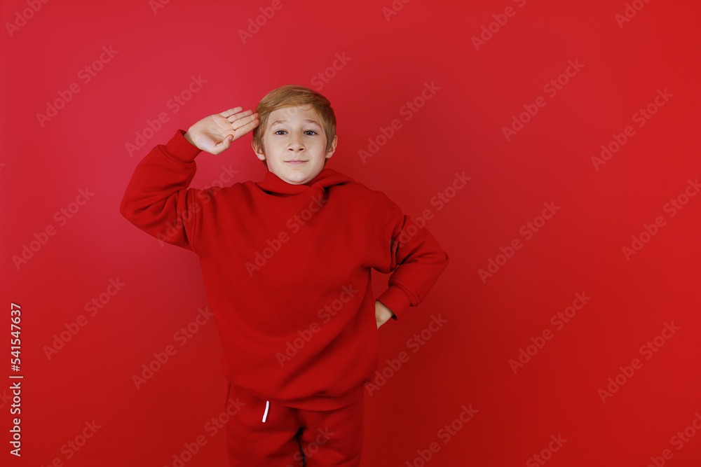 on a red background stands a boy dressed in a red suit who put his hand to his head on a red background stands a boy dressed in a red suit who put his hand to his head